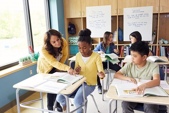 Four students at desks work with teacher.