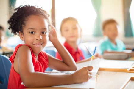 Girl writing in class with other students in the background