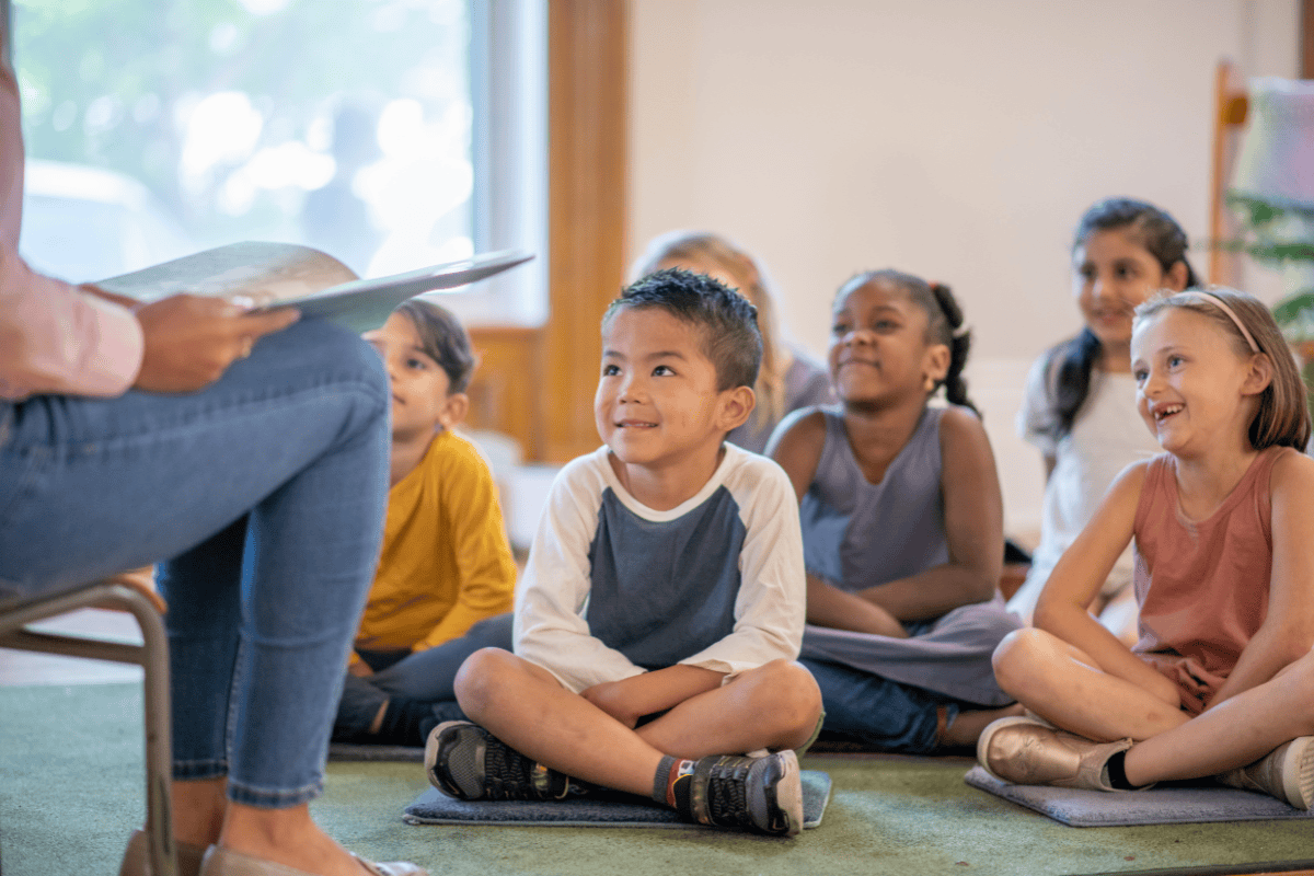 Teacher reading aloud to students sitting on the floor of the classroom